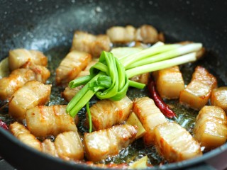 红烧肉炖土豆,再放入葱结，调适量生抽、老抽和料酒翻炒均匀至五花肉上色